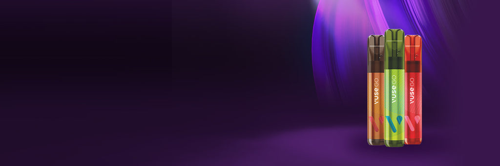 Tres vaporizadores de colores -verde, amarillo y rojo- están de pie sobre un fondo morado con rayas de luz abstractas en la esquina superior derecha. La parte izquierda de la imagen está oscura y vacía.